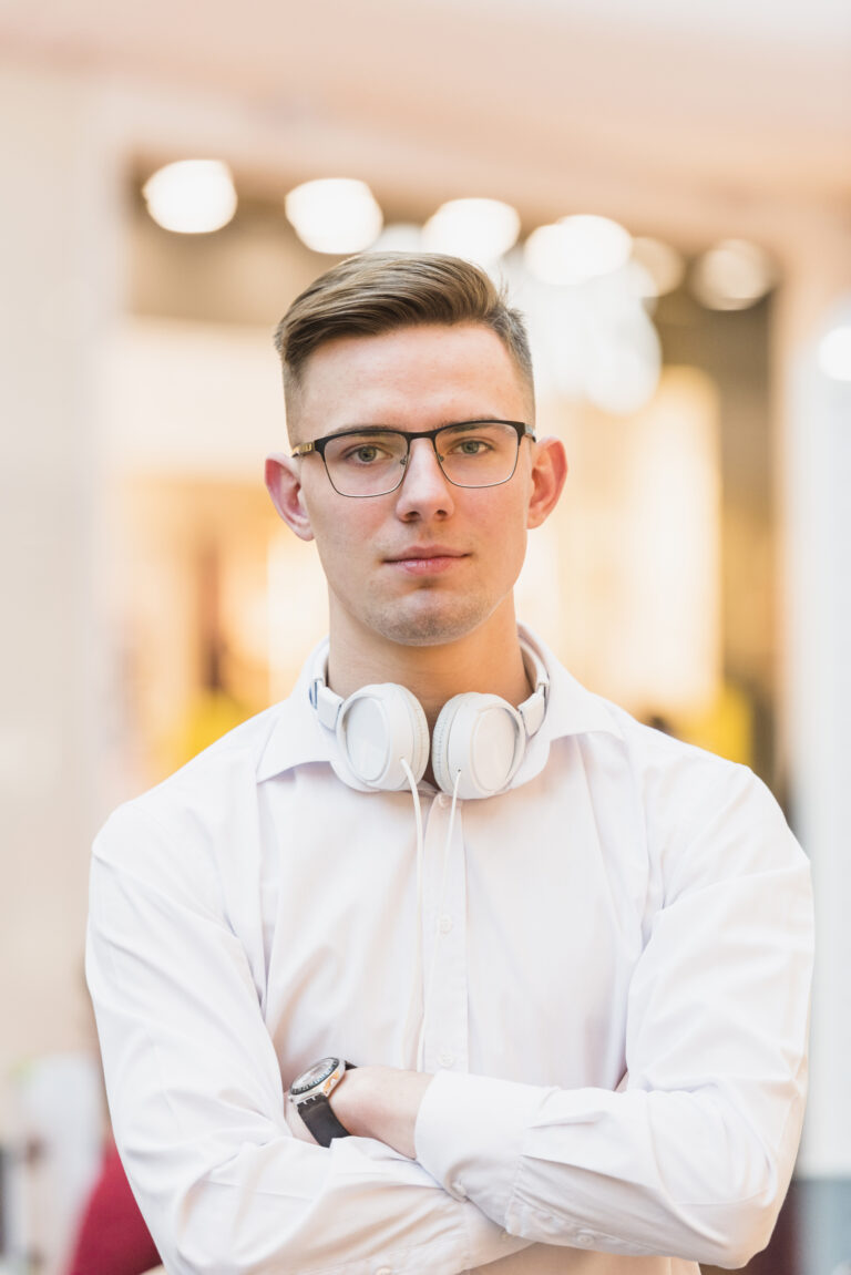 portrait-handsome-young-man-with-arms-crossed-holding-white-headphone-around-his-neck