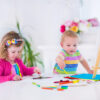 Two happy preschool children, cute little girl and funny toddler boy, painting and drawing together with water color on canvas in a sunny class room with wooden easel, creative young artists at work